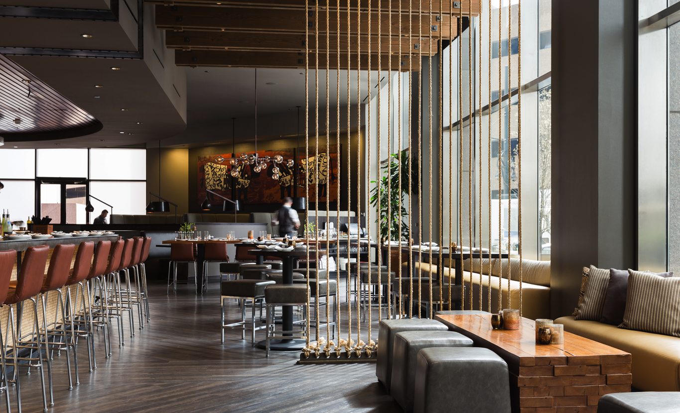 Interior of Guard and Grace in Downtown Denver featuring sleek bar seating, rope room dividers, floor-to-ceiling windows, and modern dining tables in a polished, upscale atmosphere.